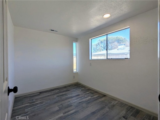 unfurnished room with a textured ceiling, wood finished floors, visible vents, and baseboards