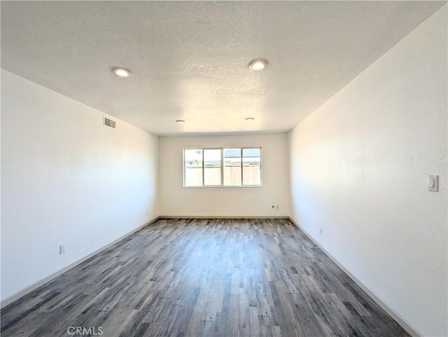 empty room with visible vents, a textured ceiling, baseboards, and wood finished floors