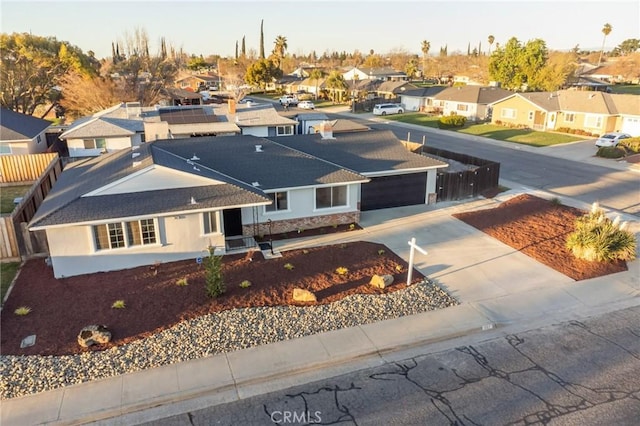 view of front of house featuring an attached garage, fence, concrete driveway, a residential view, and roof mounted solar panels