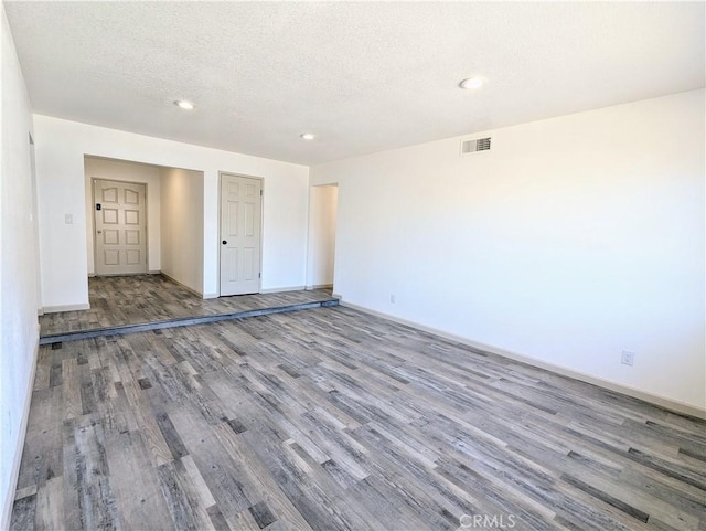 unfurnished room featuring a textured ceiling, recessed lighting, wood finished floors, visible vents, and baseboards