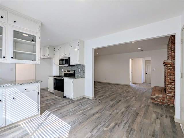 kitchen with stainless steel appliances, white cabinetry, light wood-style flooring, and decorative backsplash