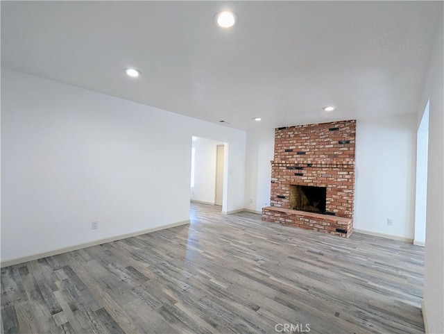 unfurnished living room with light wood-type flooring, a brick fireplace, and baseboards