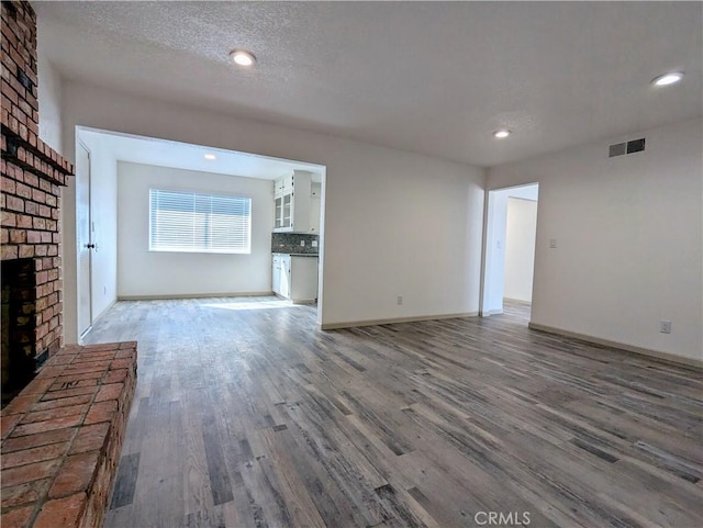 unfurnished living room featuring baseboards, visible vents, wood finished floors, a textured ceiling, and a brick fireplace