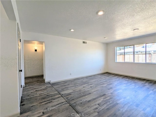 spare room with visible vents, a textured ceiling, baseboards, and wood finished floors