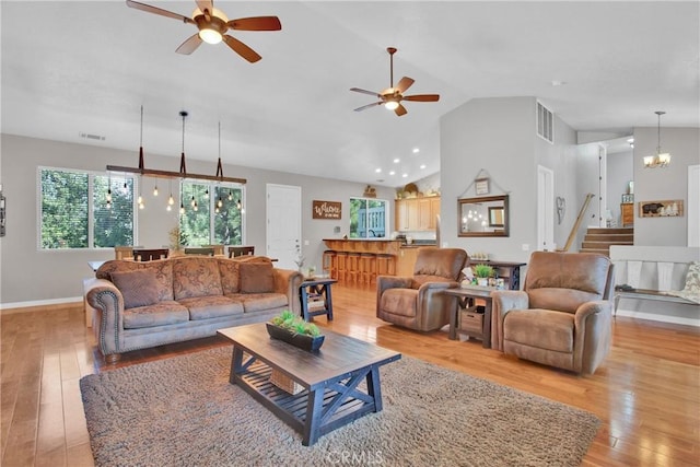 living area with visible vents, baseboards, light wood-style floors, and ceiling fan with notable chandelier
