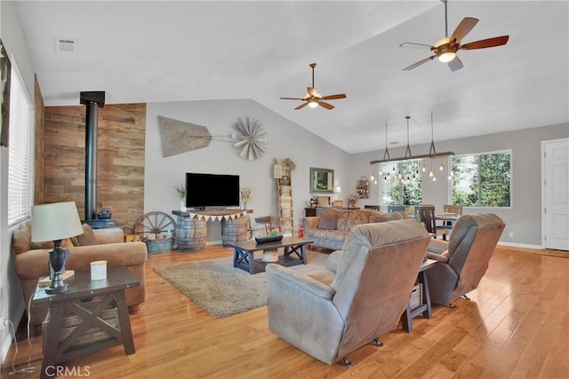living area featuring a ceiling fan, visible vents, lofted ceiling, a wood stove, and light wood-type flooring