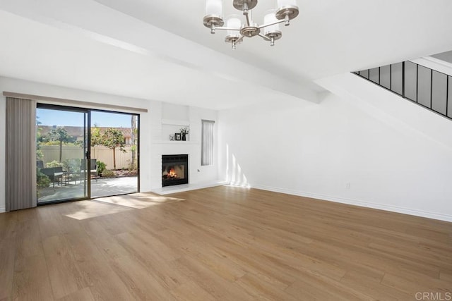 unfurnished living room with beam ceiling, an inviting chandelier, light wood-style flooring, and baseboards