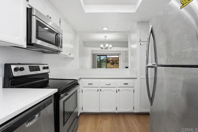 kitchen with light wood-style flooring, stainless steel appliances, white cabinetry, light countertops, and an inviting chandelier