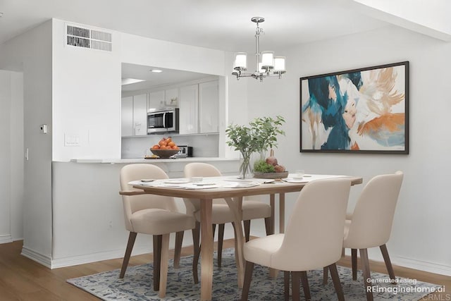 dining area featuring baseboards, a notable chandelier, visible vents, and wood finished floors