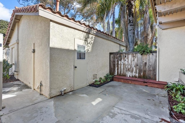 view of side of home with a tiled roof, a patio area, fence, and stucco siding