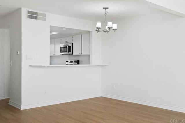 kitchen featuring stainless steel microwave, stove, wood finished floors, and visible vents