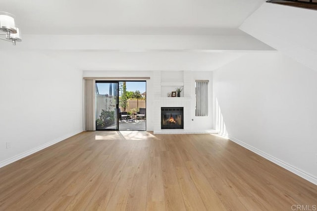 unfurnished living room featuring light wood-style floors, a brick fireplace, baseboards, and beam ceiling