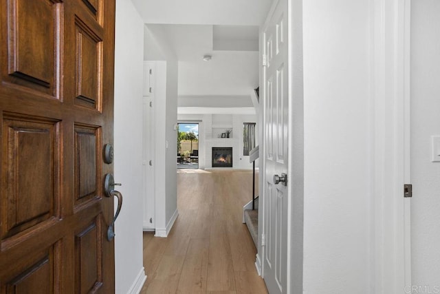 foyer entrance with baseboards, a glass covered fireplace, and light wood-style floors