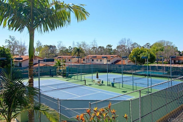 view of tennis court featuring a residential view and fence