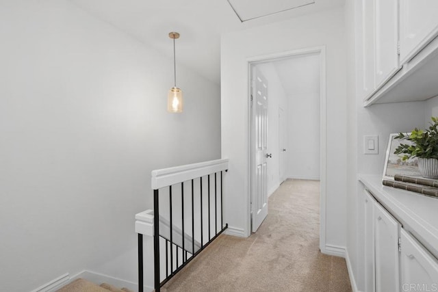 corridor with an upstairs landing, light colored carpet, and baseboards