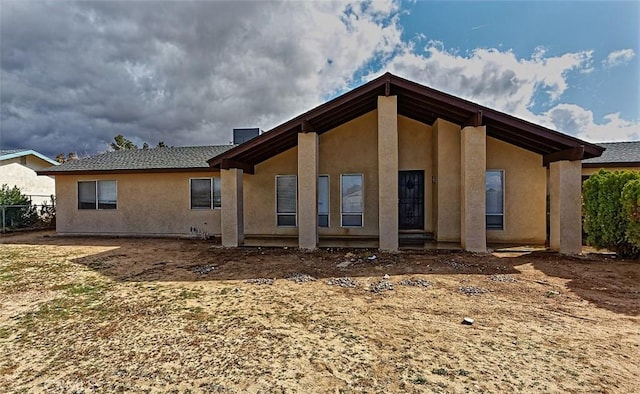 rear view of house with stucco siding and fence