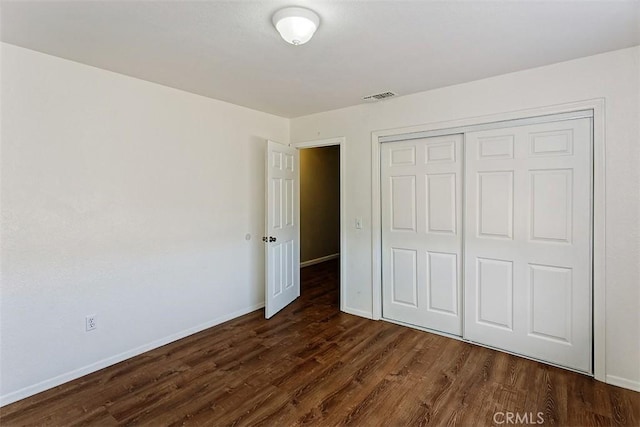 unfurnished bedroom featuring a closet, visible vents, dark wood-type flooring, and baseboards