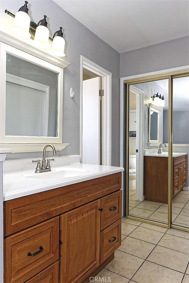 bathroom with tile patterned flooring, toilet, two vanities, and a sink