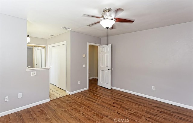 empty room featuring wood finished floors, a ceiling fan, visible vents, and baseboards