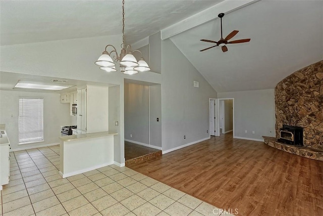 unfurnished living room featuring light tile patterned floors, beamed ceiling, baseboards, and ceiling fan with notable chandelier