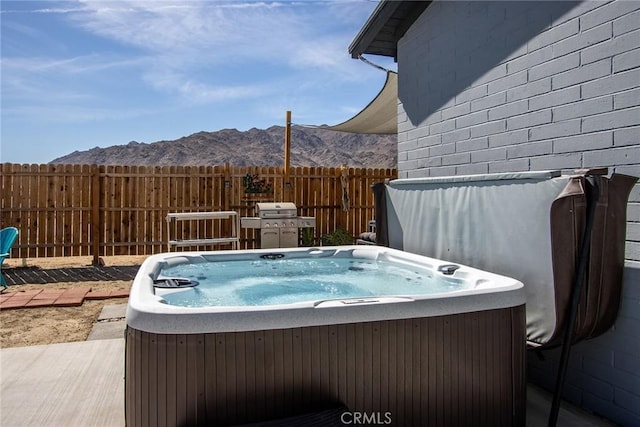 view of pool with area for grilling, fence, a mountain view, and a hot tub