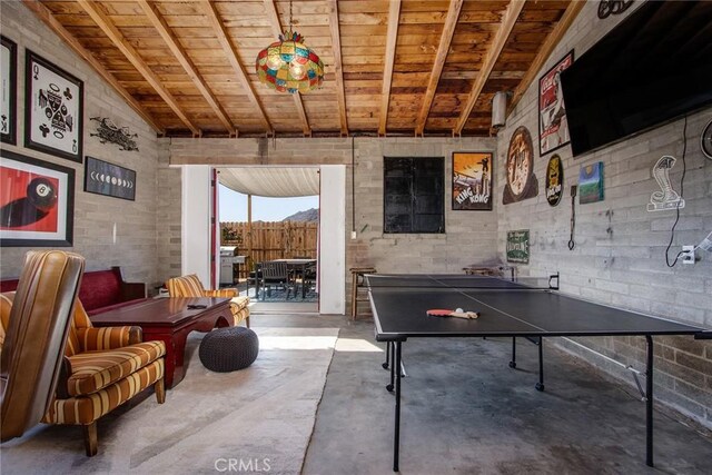 playroom featuring concrete floors, wooden ceiling, vaulted ceiling with beams, and brick wall