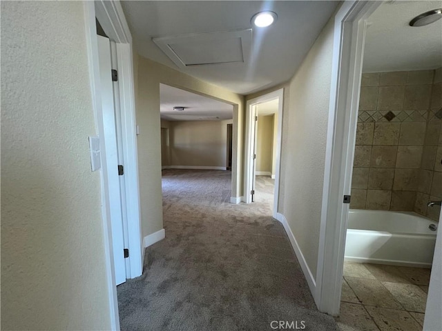 corridor featuring a textured wall, attic access, baseboards, and carpet floors