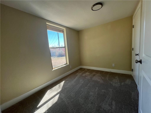 unfurnished room featuring baseboards and dark colored carpet