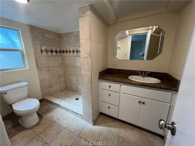 bathroom featuring vanity, baseboards, a tile shower, stone tile flooring, and toilet