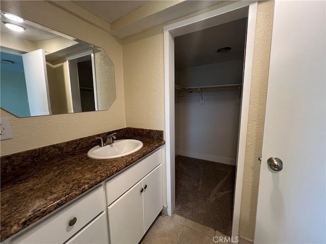 bathroom with tile patterned flooring, vanity, a walk in closet, and a textured wall