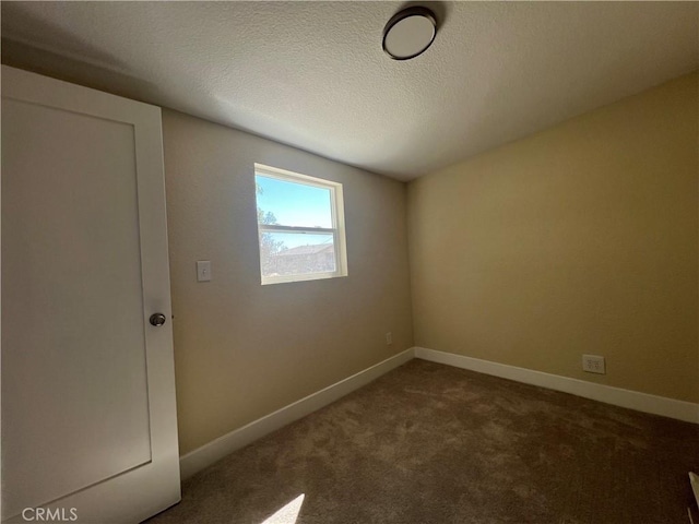 empty room with a textured ceiling, baseboards, and dark colored carpet