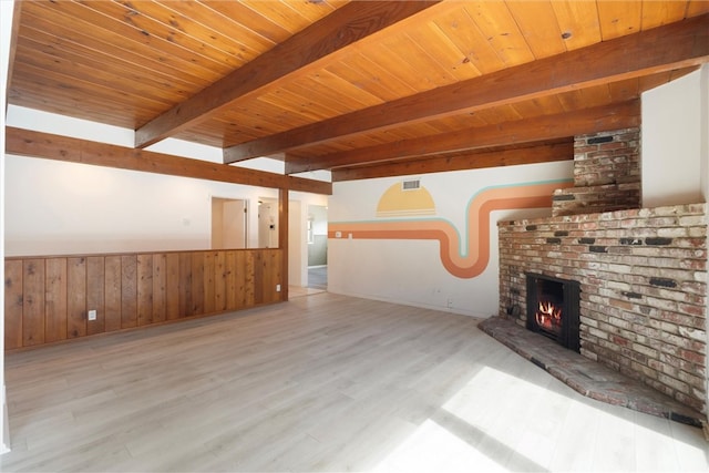 unfurnished living room featuring wooden ceiling, a wainscoted wall, wood finished floors, a brick fireplace, and beam ceiling