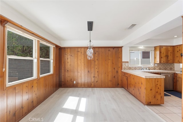 kitchen featuring tasteful backsplash, visible vents, brown cabinetry, a peninsula, and wood walls