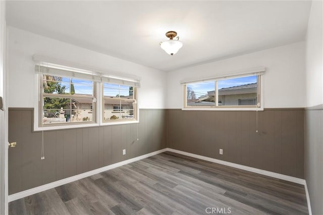 spare room with baseboards, wood finished floors, and wainscoting