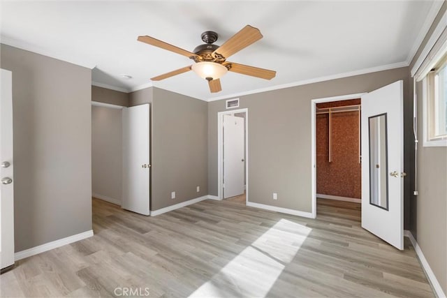 unfurnished bedroom featuring light wood-type flooring, a walk in closet, visible vents, and ornamental molding