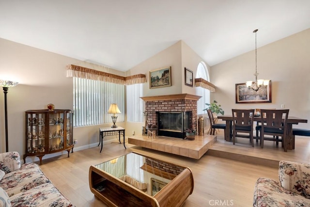 living room with a chandelier, a brick fireplace, wood finished floors, and vaulted ceiling