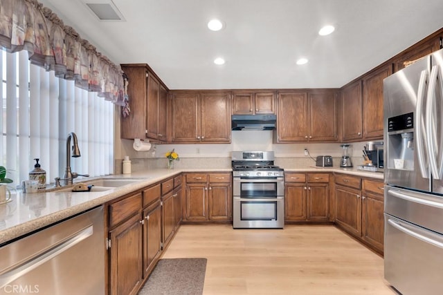 kitchen featuring a sink, light wood-style flooring, under cabinet range hood, and stainless steel appliances