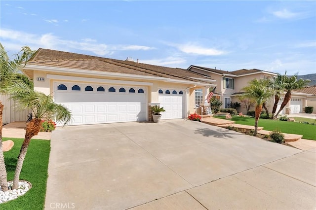 view of front of house with stucco siding, an attached garage, driveway, and a tile roof