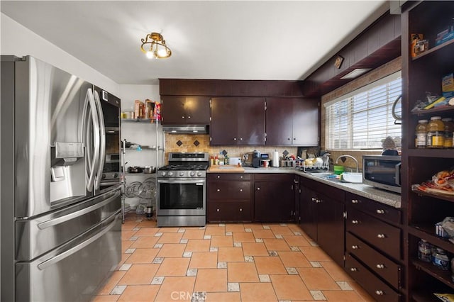 kitchen featuring tasteful backsplash, under cabinet range hood, light countertops, appliances with stainless steel finishes, and a sink