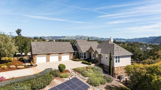 view of front of property with a garage, stone siding, a mountain view, and concrete driveway