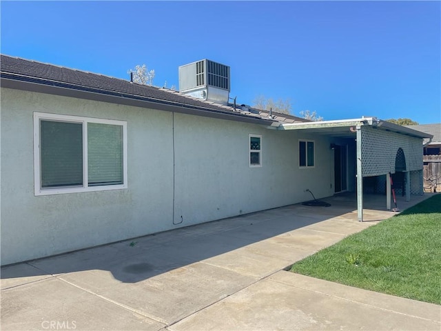 rear view of property with stucco siding, a lawn, and central air condition unit