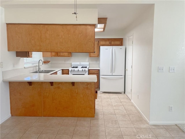 kitchen with brown cabinets, light countertops, a sink, white appliances, and a peninsula