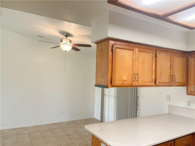 kitchen featuring baseboards, ceiling fan, brown cabinets, a peninsula, and light countertops