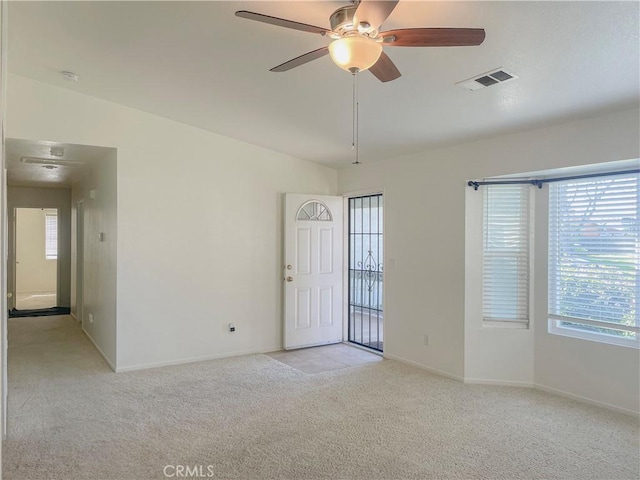 spare room featuring ceiling fan, light colored carpet, visible vents, baseboards, and vaulted ceiling