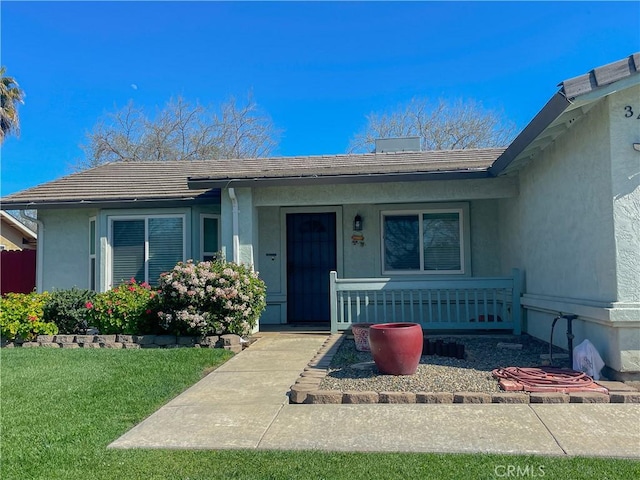 property entrance featuring covered porch, stucco siding, and a yard