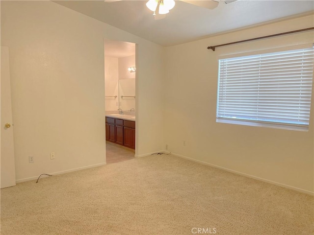 unfurnished bedroom with baseboards, light colored carpet, lofted ceiling, ensuite bath, and a sink