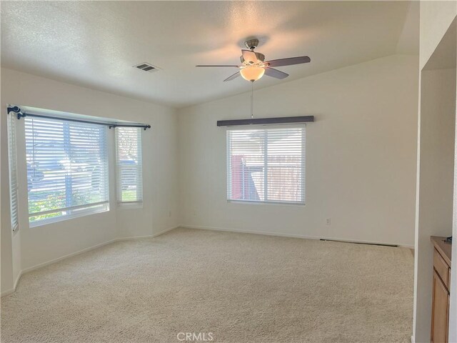 spare room featuring ceiling fan, a textured ceiling, light carpet, visible vents, and vaulted ceiling