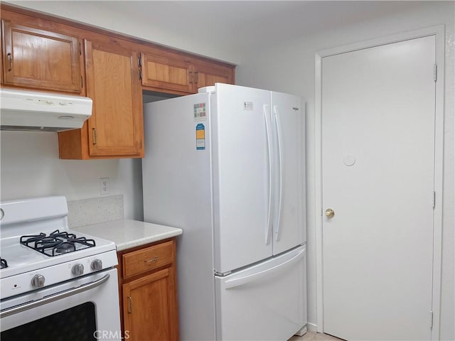 kitchen with brown cabinets, white appliances, light countertops, and under cabinet range hood