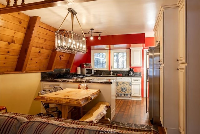 kitchen featuring beam ceiling, appliances with stainless steel finishes, a peninsula, an inviting chandelier, and dark wood-style flooring