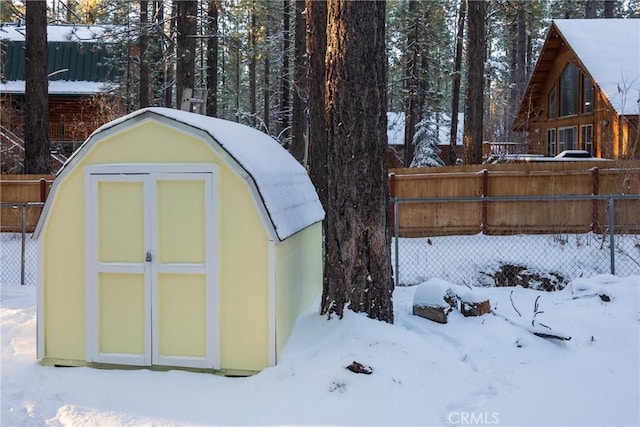 snow covered structure featuring an outdoor structure and fence